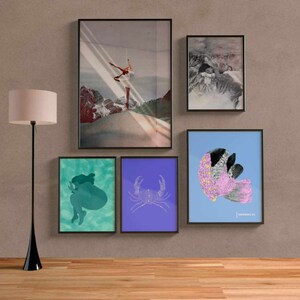 May include: Five framed prints on a beige wall. The prints are of various sizes and feature different designs. One print features a woman in a white dress dancing on a snowy mountain. Another print features a pink and white fish with black markings. The other prints feature abstract designs in blue, green, and purple.