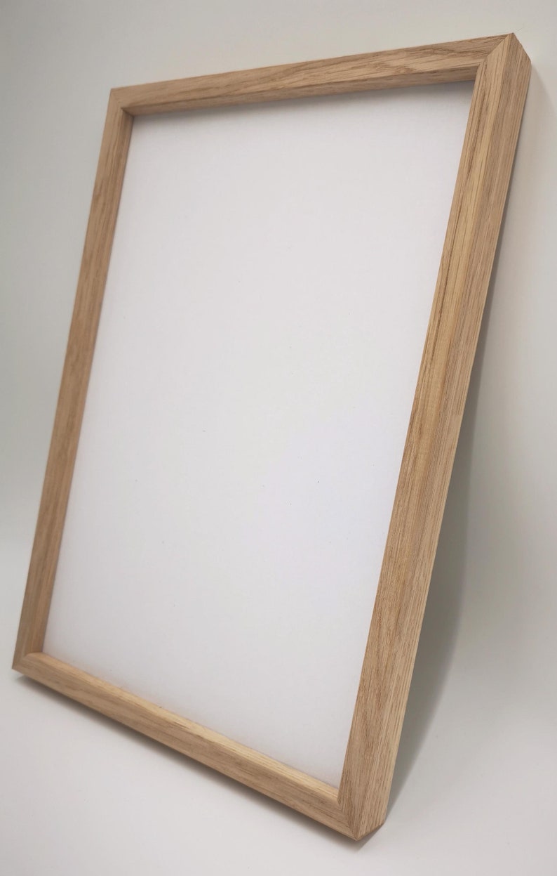 Op de afbeelding: Een fotolijst van natuurlijk hout met een lichtbruine afwerking. De lijst is vierkant en heeft een eenvoudig ontwerp.