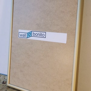 May include: A gold-colored picture frame with a light brown backing. The frame has a sticker on the front that says "wall &hearts; bonito".
