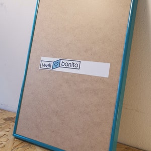 May include: A teal picture frame with a brown backing. The frame has a white sticker with the text "wall &hearts; bonito" on it.