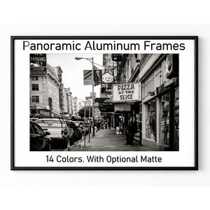 May include: A black aluminum frame containing a black and white photograph of a city street with cars and a sign reading PIZZA BY THE SLICE. The text Panoramic Aluminum Frames and 14 Colors. With Optional Matte is printed on the white border.