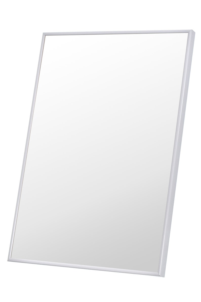 May include: A rectangular mirror with a white frame. The mirror is angled slightly, showcasing its reflective surface. The frame is a simple, clean design, suitable for various decor styles.