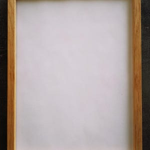 May include: A rectangular wooden picture frame with a light brown finish. The frame has a simple, clean design and surrounds a white interior. The frame is empty, ready to hold a photograph or artwork.