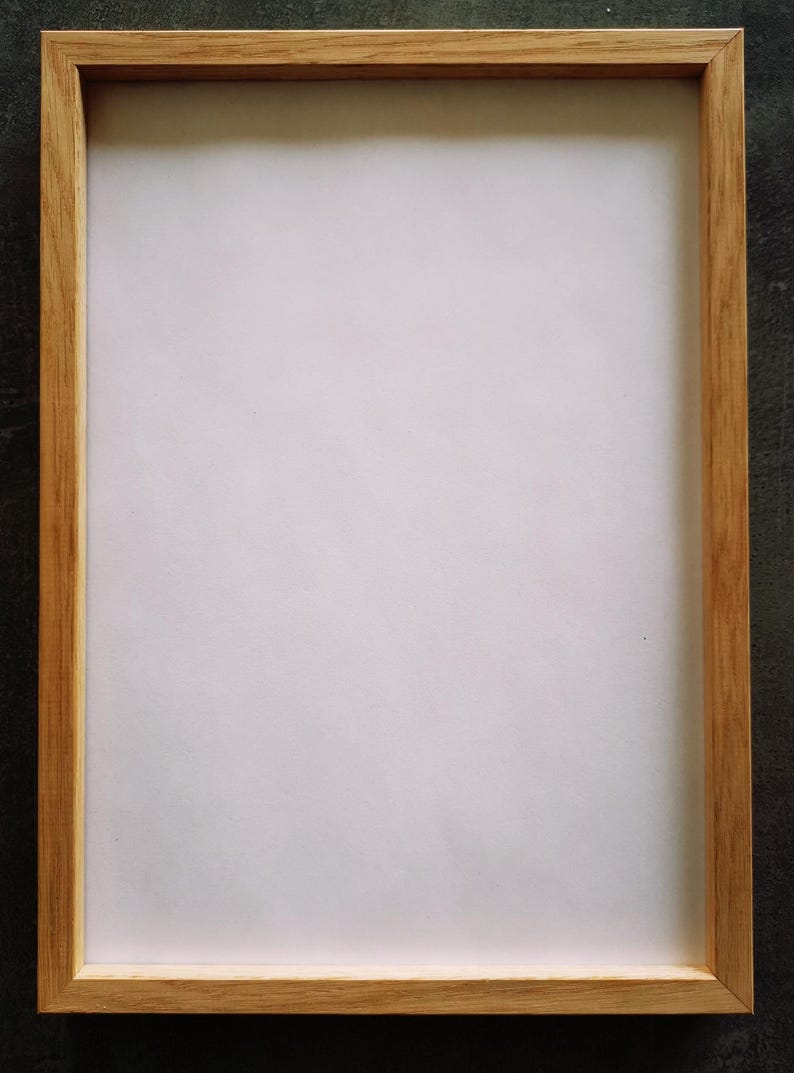 May include: A rectangular wooden picture frame with a light brown finish. The frame has a simple, clean design and surrounds a white interior. The frame is empty, ready to hold a photograph or artwork.