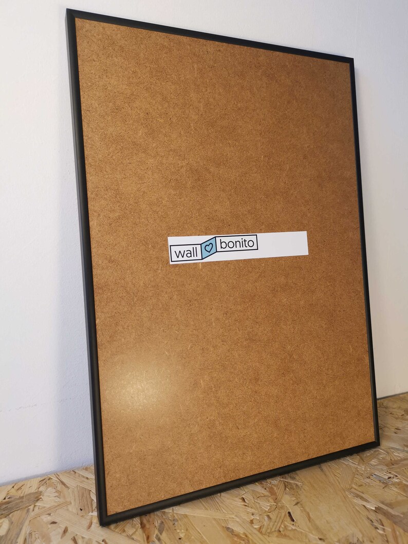 May include: A black framed picture with a brown wood backing. The frame is on a wooden surface. A sticker on the backing says "wall &hearts; bonito".