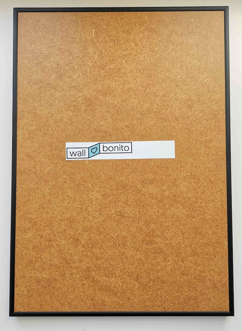 May include: A brown corkboard with a black frame. A white sticker with the text "wall &hearts; bonito" is attached to the corkboard.