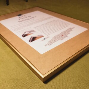 May include: A gold-colored picture frame with a brown mat. The frame has a simple, modern design. The text "Art & Pictures belong here" is printed on the mat.