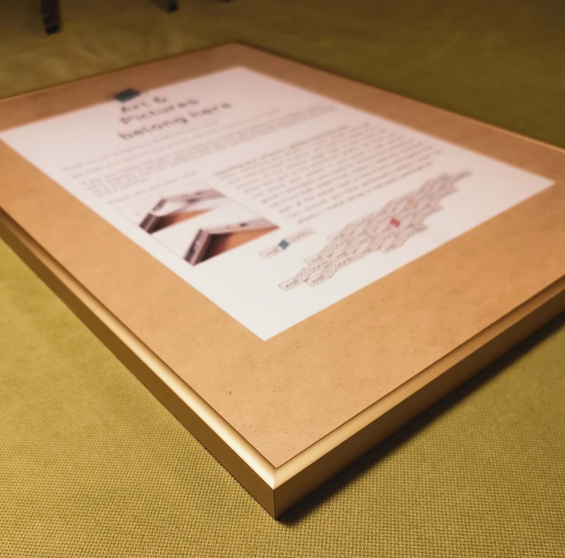 May include: A gold-colored picture frame with a brown mat. The frame has a simple, modern design. The text "Art & Pictures belong here" is printed on the mat.
