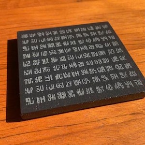 May include: Black square coaster with white text. The text is in a stylized font and reads: "HP UIJI JY VEIKIMO SH 318 : 4 2005 SHAMO IF as 'n 20150 新品 18 21 10 Pa HS N"