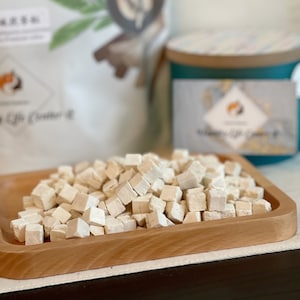 May include: A wooden tray filled with small, white, cube-shaped pieces of dried fruit. The tray is on a white surface.