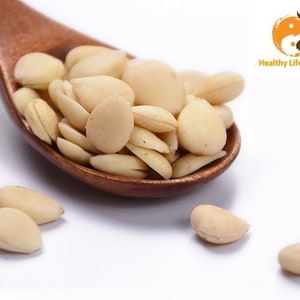 May include: A wooden spoon filled with white almond kernels. The almonds are arranged in a random pattern. There are also a few almonds scattered on a white surface.