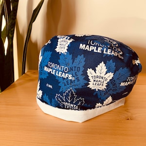 May include: A blue and white fabric scrub hat with a repeated pattern of the Toronto Maple Leafs logo. The hat has a white brim and the text "TORONTO MAPLE LEAFS®" is visible on the hat.