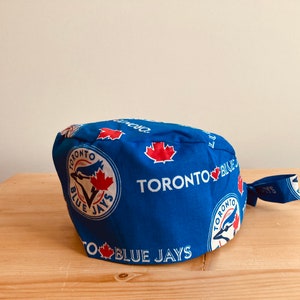May include: A blue Toronto Blue Jays baseball cap with a white and red logo and text. The cap features a maple leaf design and the words "Toronto Blue Jays". The cap is made of fabric and has a tie closure.