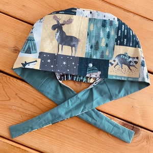 Peut inclure: Un bonnet de chirurgien fait à la main avec un motif patchwork représentant des animaux de la forêt et des arbres. Le bonnet a une attache vert teal et une doublure à motifs blancs et teal. Le motif comprend un orignal, un raton laveur et un ours.
