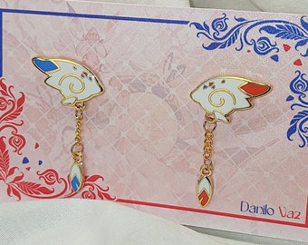 May include: A pair of gold-tone earrings with white and blue enamel designs. The earrings feature a small, stylized animal with a red, white, and blue tail. The earrings are displayed on a white card with a red and blue floral design. The card also includes the text "Danilo Vaz".
