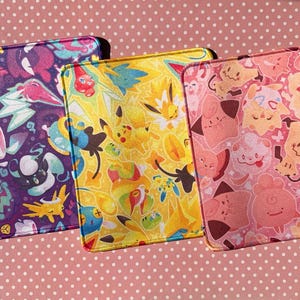 Puede incluir: Tres alfombrillas de ratón coloridas con diferentes personajes de Pokémon. La primera alfombrilla de ratón es morada con un diseño azul claro y rosa. La segunda alfombrilla de ratón es amarilla con un diseño azul claro y rosa. La tercera alfombrilla de ratón es rosa con un diseño azul claro y amarillo.
