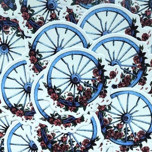 May include: A collection of stickers featuring a blue wagon wheel design. Each wheel is adorned with red roses and green leaves. The stickers have a white background and a vintage aesthetic.