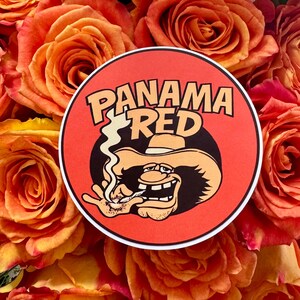 May include: A round sticker with the words "PANAMA RED" in orange lettering. The sticker features a cartoon character wearing a hat and smoking. The background is a bouquet of orange roses.
