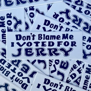 May include: White bumper stickers with dark blue text that reads "Don't Blame Me I Voted For Jerry." The stickers are rectangular and feature a retro font. Other stickers with similar text are scattered around.