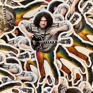 May include: A collection of stickers featuring a musician playing a black guitar. The musician is wearing a gray sweater, rainbow-colored pants, and brown shoes. The stickers have a white border.