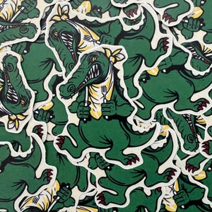 May include: A collection of stickers featuring a green alligator holding a fork and knife. The alligator has a yellow bandana and is set against a white background. The stickers have a cartoon style.