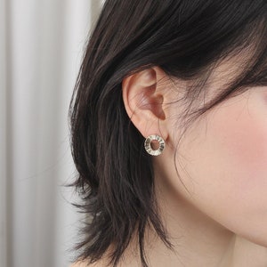 May include: Gold hoop earrings with a textured design. The earrings are small and delicate.
