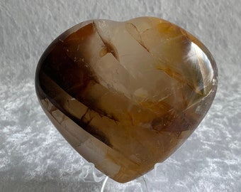 May include: A heart-shaped crystal with brown and white banding. The crystal is on a clear stand.