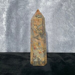 Puede incluir: Un cristal puntiagudo multicolor con remolinos de marrón, rojo y blanco. El cristal está sobre una superficie negra.