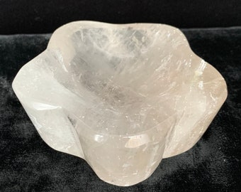 May include: A clear quartz crystal bowl with a star-shaped design. The bowl is smooth and polished, with a slightly cloudy appearance.
