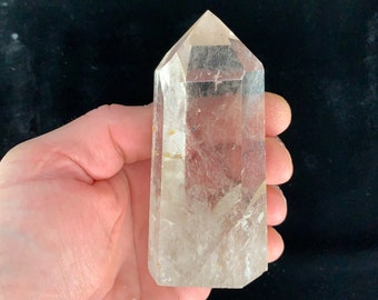 Op de afbeelding: Een heldere kwartskristalpunt met een natuurlijke, gefacetteerde vorm. De kristal is ongeveer 7,6 cm hoog en heeft een glad, gepolijst oppervlak.