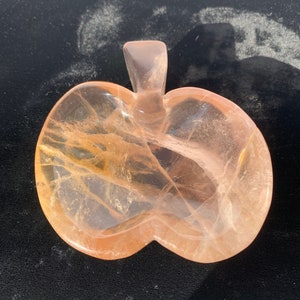 May include: A carved crystal apple with a light pink and orange hue. The crystal is translucent and has a natural, organic look.