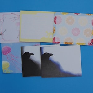 Könnte beinhalten: Fünf leere Grußkarten mit verschiedenen Designs. Die Karten sind alle weiß mit verschiedenen farbigen Designs. Die Designs umfassen ein Blumenmuster, ein Zitrusmuster, eine Krähen-Silhouette und ein Quallenmuster.