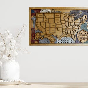 May include: A wooden map of the United States with a "Our Family Travel Map" inscription. The map is framed in a light brown wood frame and has a detailed design with various landmarks and cities.