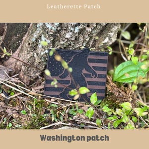 May include: A square leatherette patch featuring a silhouette of Bigfoot walking across a brown and black American flag design. The text "Washington patch" is at the bottom, and "Leatherette Patch" is at the top.