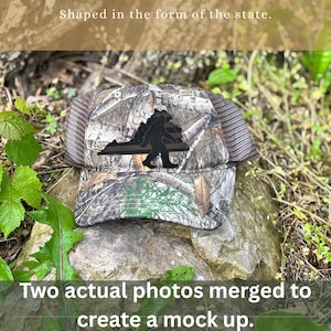 May include: Camouflage trucker hat with a black silhouette of Bigfoot and the shape of a state. The hat has a mesh back and a curved brim. The text "Shaped in the form of the state" and "Two actual photos merged to create a mock up" are visible.