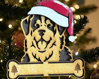 May include: Wooden Christmas ornament featuring a dog wearing a Santa hat. The dog's face is intricately carved with black accents, and the ornament includes a bone-shaped tag with a Christmas tree design. The ornament is hanging on a Christmas tree.