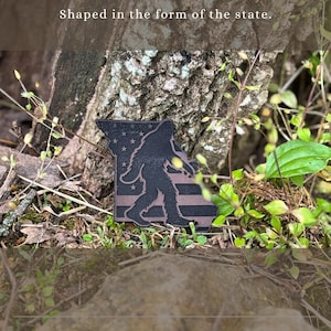 May include: A wooden patch shaped like the state of Missouri, featuring a Bigfoot silhouette and a flag design. The patch is dark brown with a lighter brown striped pattern and stars. The text "Shaped in the form of the state" is at the top.