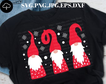 Könnte beinhalten: Ein schwarzes T-Shirt mit drei roten Gnomen, die weiße Hüte und weiße Bärte tragen. Die Gnome sind in einer Reihe angeordnet, wobei der Gnome links ein rot-weißes Punkte-Muster trägt, der Gnome in der Mitte ein rot-weißes Punkte-Muster trägt und der Gnome rechts ein rot-weißes Dreiecksmuster trägt. Das T-Shirt ist mit weißen Schneeflocken und weißen Punkten verziert.