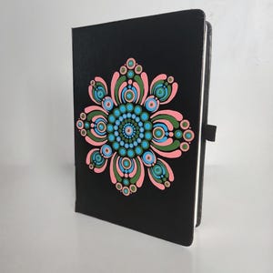 May include: Black notebook with a pink, green and blue mandala design painted on the front cover.