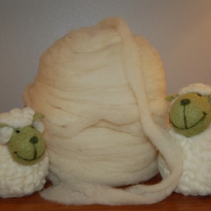 May include: Two white felt sheep figurines with green faces, sitting next to a large ball of white wool.