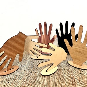 May include: Five wooden hand-shaped sculptures, each with a different wood grain and color. The hands are arranged in a semi-circle, with the tips of the fingers touching. The sculptures are all on small wooden bases.