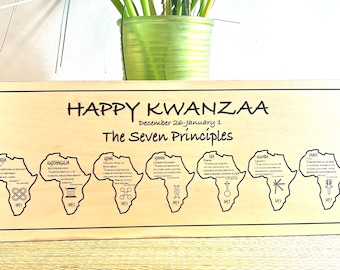May include: A wooden sign with the words "Happy Kwanzaa" and "The Seven Principles" in black lettering. The sign features seven outlines of the continent of Africa, each with a different symbol and text describing the principle for each day of Kwanzaa.