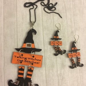 Puede incluir: Un conjunto de joyas con temática de Halloween que incluye un collar y dos pendientes. El colgante del collar y los pendientes tienen forma de sombreros de bruja con bandas naranjas y piernas negras con medias a rayas naranjas y negras. El collar tiene el texto "Talking Witches Get Stitches!"