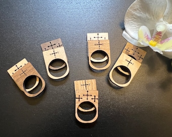 May include: Five wooden rings with a compass design. Each ring has a cross with the letters N, S, E, and W engraved on it. The rings are stacked on top of each other.
