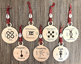 May include: Seven wooden ornaments with red and white ribbon, each featuring a different African Adinkra symbol and its corresponding meaning. The symbols include Umoja (Unity), Sankofa (Self Determination), Nyame (Collective Work and Responsibility), Yaa (Cooperative Economics), Na (Purpose), Kumbira (Creativity), and Imani (Faith).