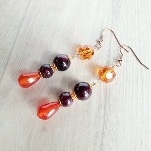 May include: A pair of dangle earrings with orange and dark red beads. The earrings have gold-toned hooks and are made with faceted glass beads.