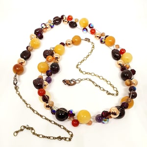 Puede incluir: Un collar de múltiples hilos con una mezcla de cuentas amarillas, naranjas, rojas, marrones y moradas. El collar está hecho con un alambre y una cadena.