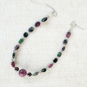 Könnte beinhalten: Eine silberne Kettenkette mit grünen und rosafarbenen Edelsteinperlen. Die Perlen sind oval geformt und haben eine marmorierte Optik.