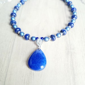May include: A blue lapis lazuli gemstone pendant necklace with silver beads and a silver chain. The pendant is a teardrop shape and has a sparkly silver accent.