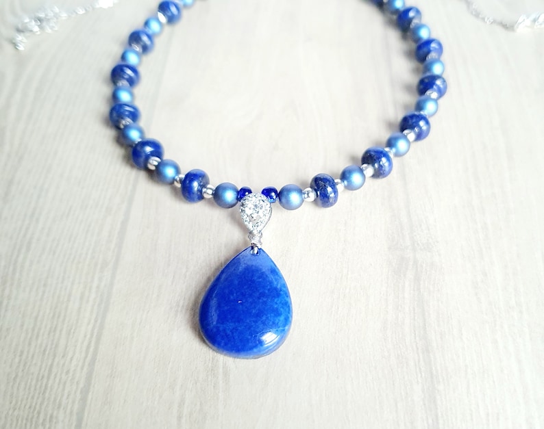 May include: A blue lapis lazuli gemstone pendant necklace with silver beads and a silver chain. The pendant is a teardrop shape and has a sparkly silver accent.